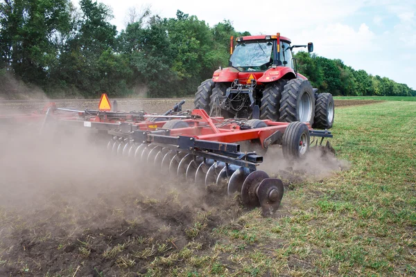 Modern tech red tractor plowing a green agricultural field in spring on the farm. Harvester sowing wheat.