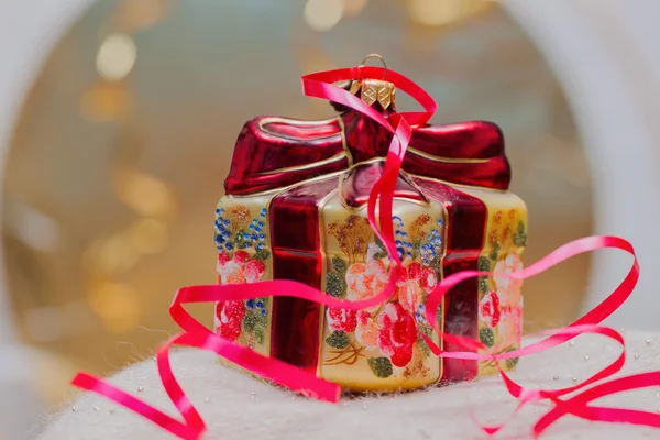 Close up of decorative Christmas decoration at a gift box with red ribbons on gold blurred background. Selective focus