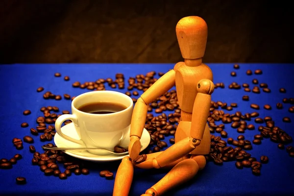Coffee cup and coffee beans with wooden figure on wooden table