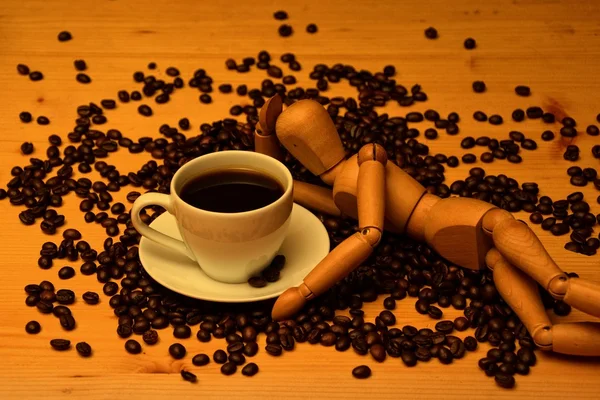 Coffee cup and coffee beans with wooden figure on wooden table