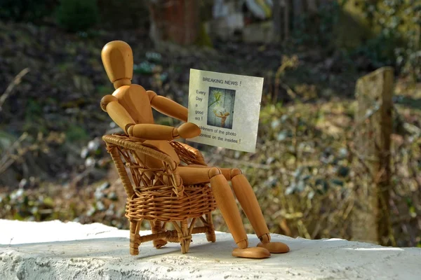 Wooden figure sitting on patio chair and reading newspaper