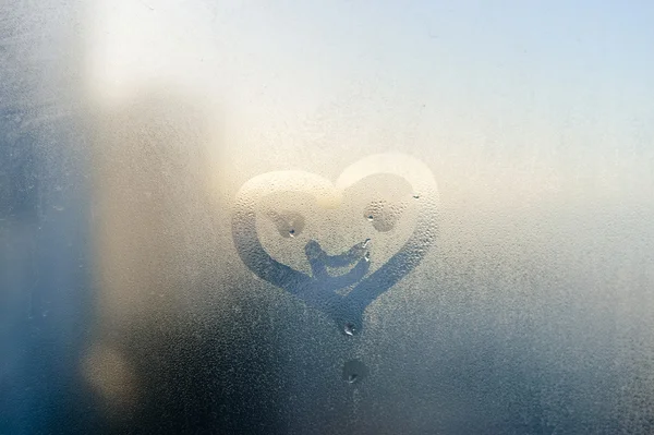 Smile face and heart drawing on window, season abstract background. Rain drops