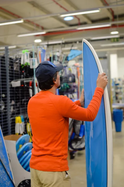 Back view of male surfer holding a surf board on shop background
