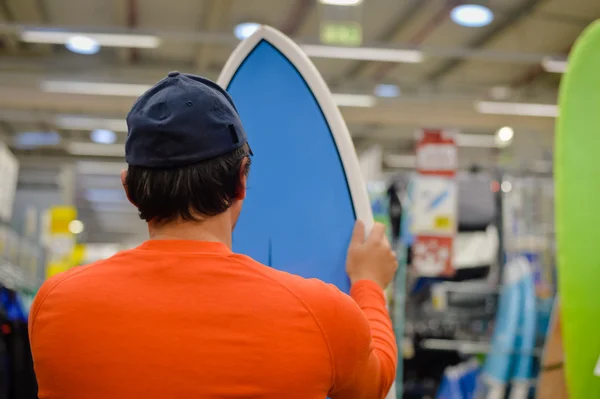 Male surfer choosing holding a surf board on shop factory background