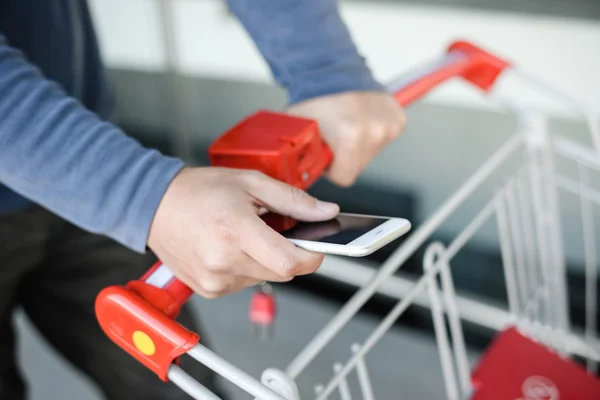 Closeup on hand holding mobile smart phone touch screen with trolley on background of department store