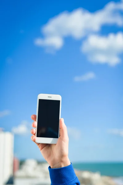 Closeup on hand holding mobile cell phone over city buildings background, blank black screen , selfie picture