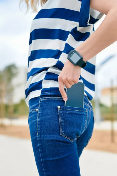 Back side view of person in jeans using smart watch with smartphone in pocket. Close up photo of mock up blank empty copy space.