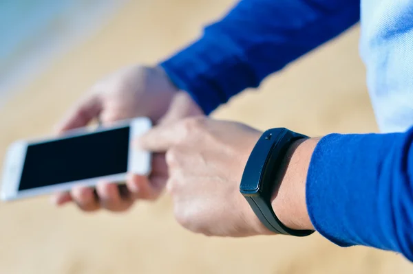 Person holding mobile phone checking connection using watch. Sea beach behind background