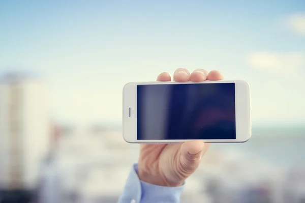 Closeup on hand holding mobile cell phone over city buildings business background.