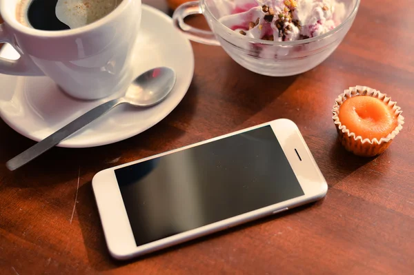 Top view of coffee cup, smart phone, icecream and cakes on wood background.