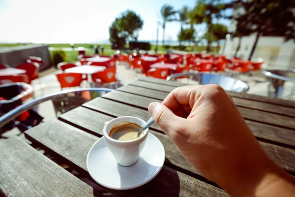A hand holding spoon for coffee cup outside in the restaurant background