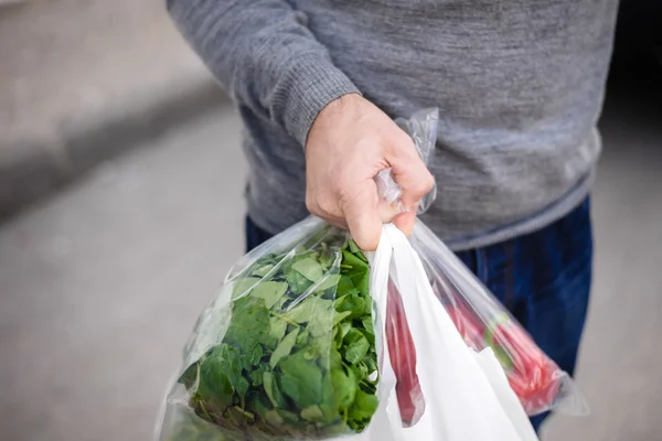 Closeup of bag full of fruits and vegetables. Male carrying bag in his hand after shopping.
