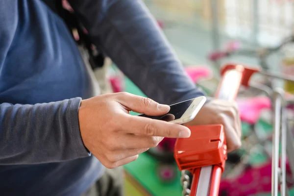 Closeup on person holding mobile phone in hand during shopping. Cart on background of store