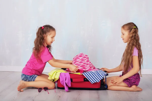 Children, two girls, gather clothes in a suitcase