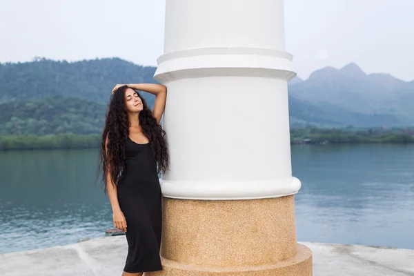 Beautiful woman in black dress with long black hair standing near lighthouse