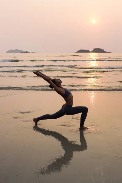 Young slim woman practicing pose from yoga on the beach at sunset