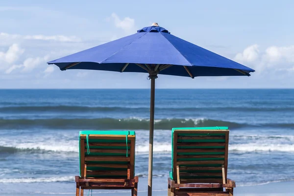 Blue umbrella with two recliners at the ocean coast