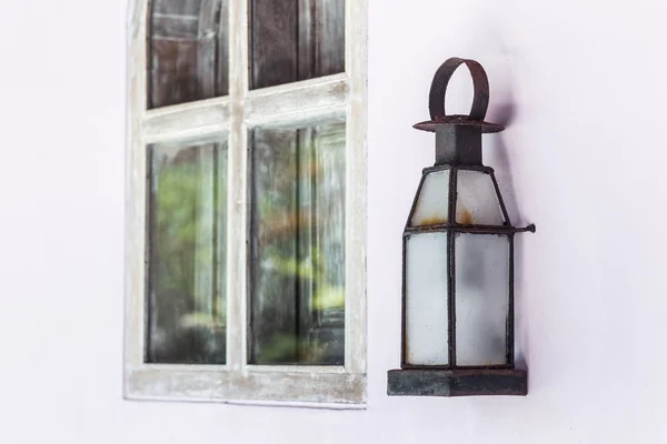 Old metal lamp on white wall near wooden window