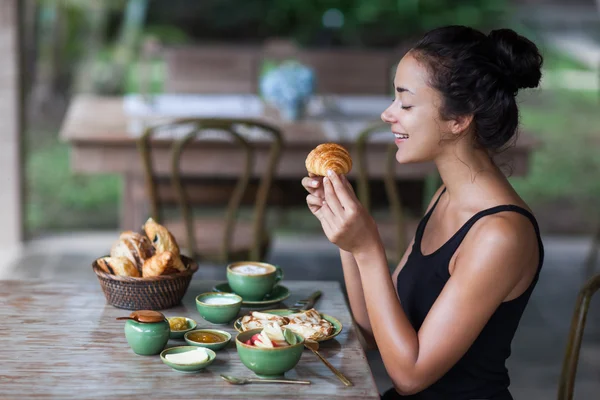 Young woman enjoying breakfast and holding croissant in hand. Morning good mood