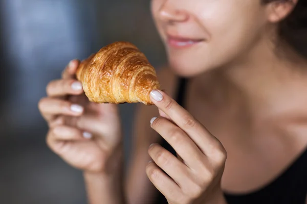 Young woman enjoying breakfast and holding croissant in hand. Morning good mood