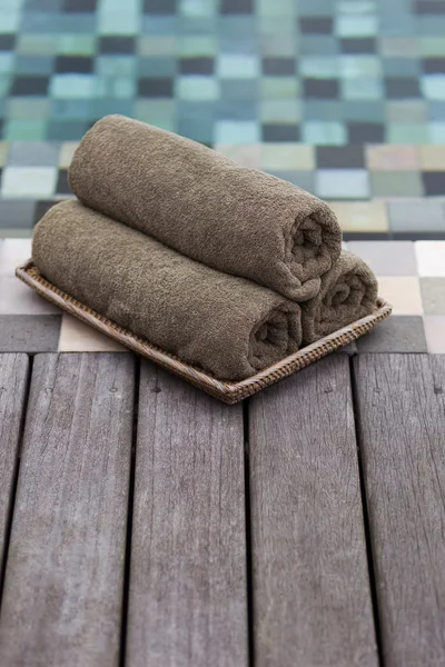 Three grey towels rolled near swimming pool.