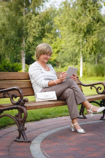 Attractive mature woman using digital tablet in a park