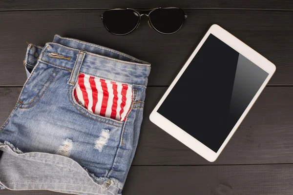 Summer women\'s accessories: shorts, tablet, sunglasses on wood background.