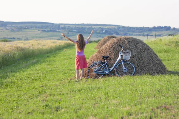 Young woman with a bicycle on field with haystacks on a sunny da