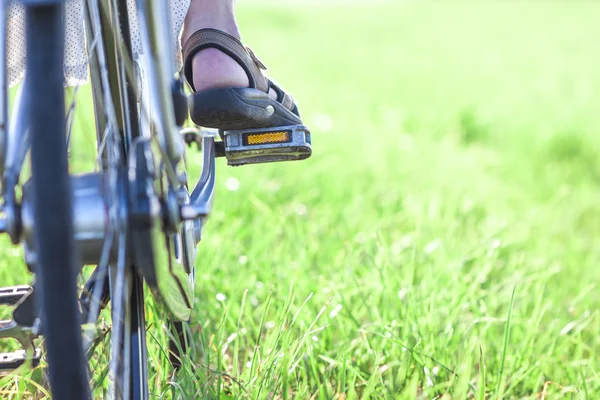 Womans foot on bicycle pedal on green grass closeup