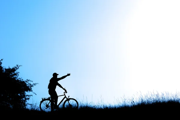 Silhouette of a man raising hand on  bicycle on blue sky