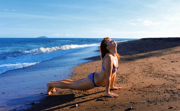 Red hair girl making yoga in swimsuit on the beach by the sea, vacation in Philippines
