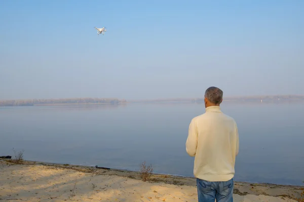A man stands on the river bank and controls the drone.