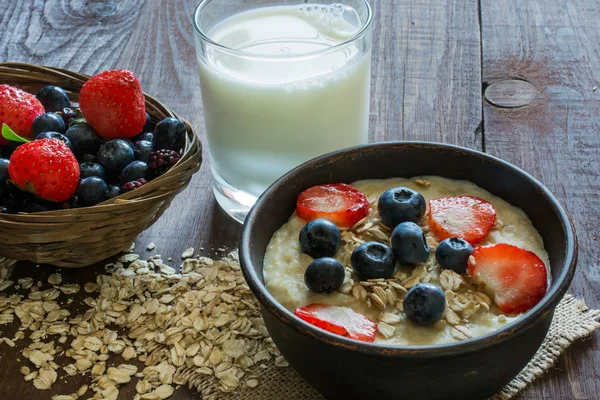 Oatmeal porridge with berries and glass of milk on wooden table