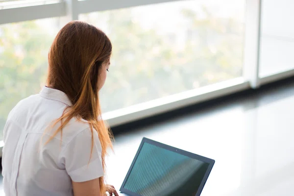 Asian woman student working on a laptop in building near window