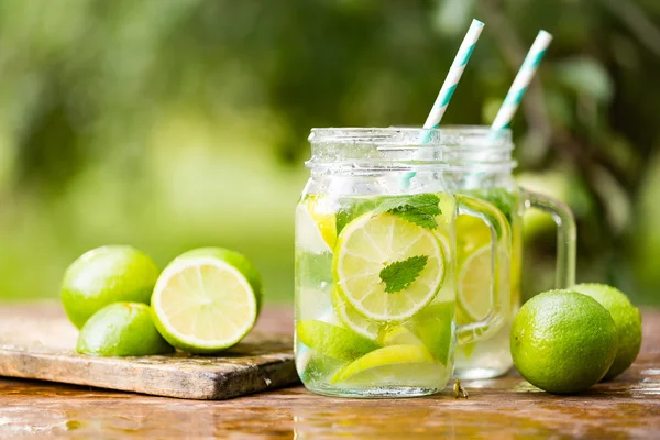 Fresh drink lemonade mojito in mason jar on wooden background. Mojitos with mint leaves, lime and ice, outdoor.