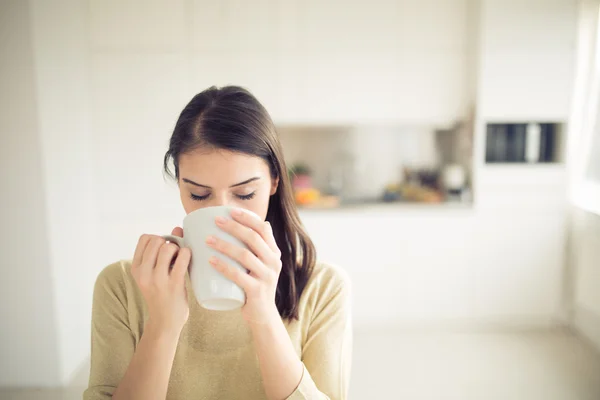 Young woman enjoying,holding cup of hot beverage,coffee or tea in morning sunlight.Enjoying her morning coffee in the kitchen.Savoring a cup of coffee breathing in the aroma