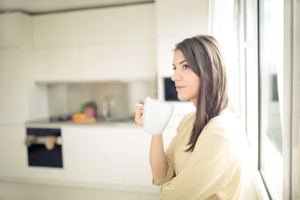 Young woman enjoying,holding cup of hot beverage,coffee or tea in morning sunlight.Enjoying her morning coffee in the kitchen