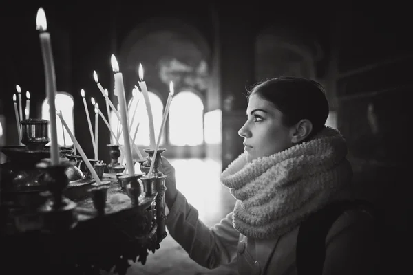 Young female lighting candles in a church during praying.Yellow votive candles burning.Woman praying to god at St. Alexander Nevsky Cathedral