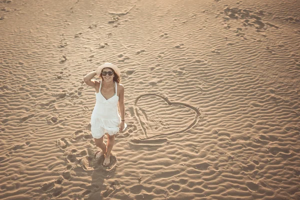 Woman on the beach making heart on the sand.Young woman walking on the sand in a white dress.Relaxed woman breathing fresh air