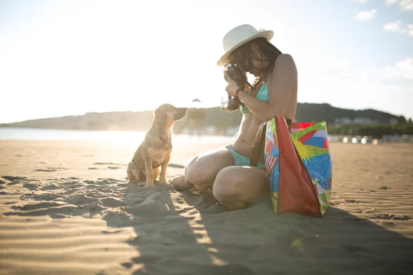 Young woman playing with dog pet on beach during sunrise or sunset.Girl and dog having fun on seaside.Woman making photo of puppy posing