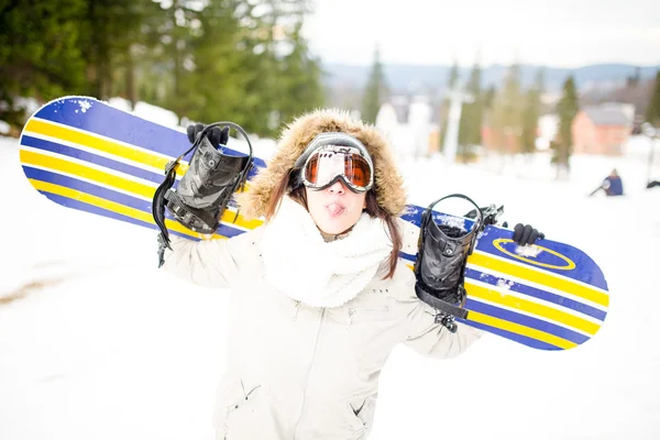 Sport woman in snowy mountains. The concept of the winter holiday. Snowboarding.Young beautiful woman with ski mask holding her snowboard at ski slope Young woman holding snowboard on her shoulders