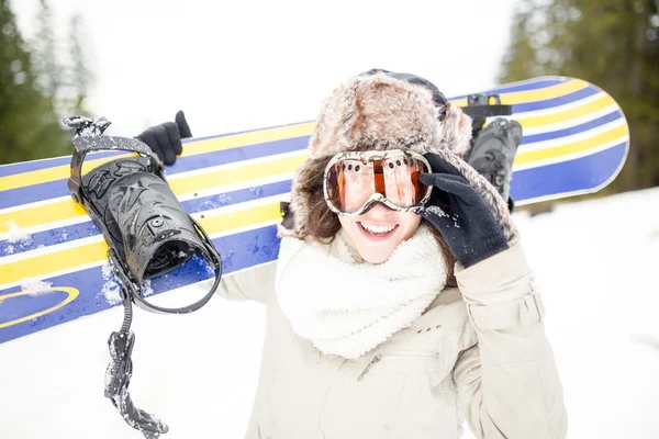 Sport woman in snowy mountains. The concept of the winter holiday. Snowboarding.Young beautiful woman with ski mask holding her snowboard at ski slope Young woman holding snowboard on her shoulders