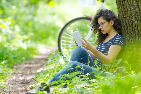 Lovely young brunette woman, reading a book in a park