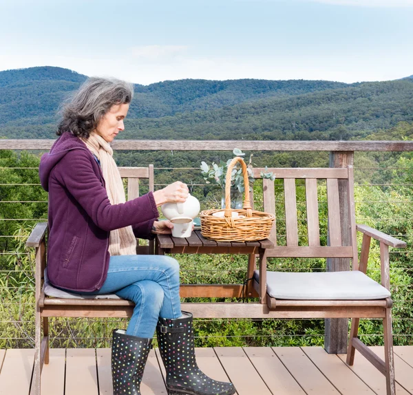 Middle aged woman pouring tea with landscape background