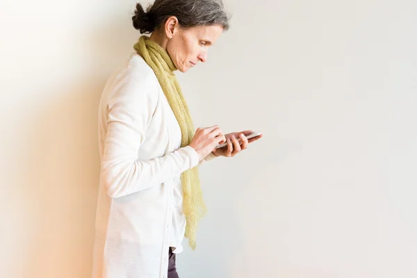 Profile of mature woman in green scarf using smart phone