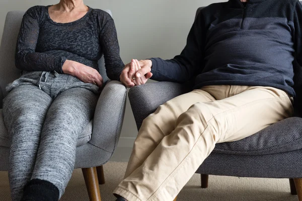 Older couple in armchairs holding hands (cropped)