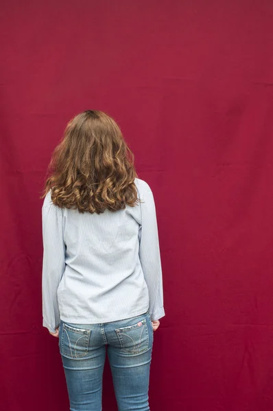 The girl in jeans and shirt stands with his back on the red back