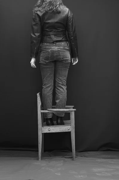 Girlish legs in torn jeans on black background. Beautiful girl balances on back of  black background. Artwork.The girl in jeans standing on a chair backwards, his head cut off. Black-and-white photo.