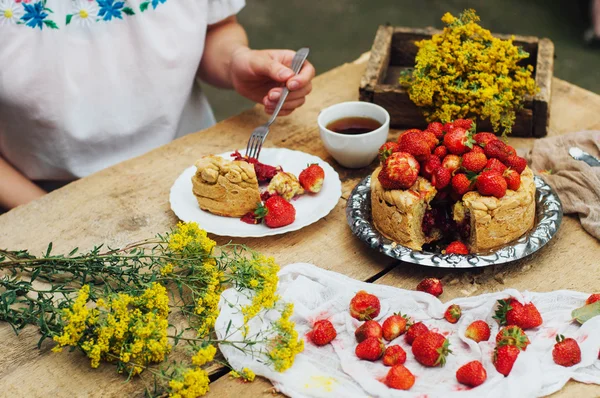 Woman eating a delicious home-made cake with aisheny and stuffed strawberries for dessert. Summer Styled dinner table. Coffee to the cake. sitting at the rustic dining table