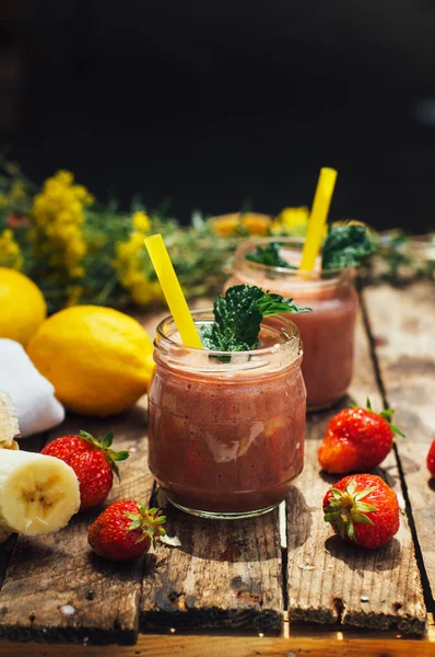 Banana and strawberry smoothie. Two Cold Strawberry Banana Smoothies in Glasses with Ingredients on Kitchen Table. Strawberry Banana Smoothie made with fresh Ingredients. Fresh strawberry  smoothie